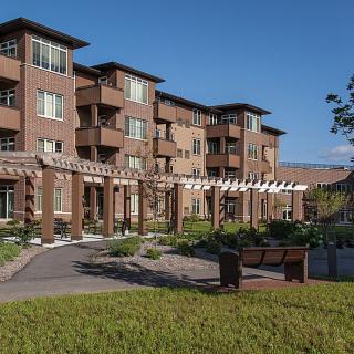 A modern residential apartment building with a landscaped garden and benches in front.