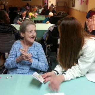 A caregiver engages in conversation with an elderly resident at a care facility.