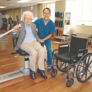 An elderly person receiving assistance from a caregiver during a rehabilitation session.