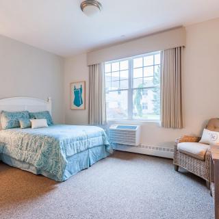 A cozy bedroom with a neatly made bed, large window, and comfortable chair.