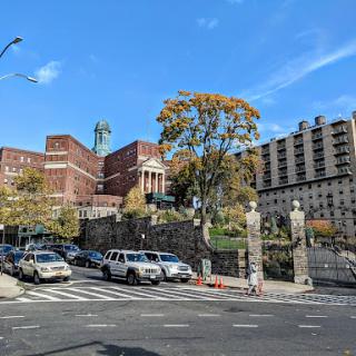 A view of a historic building with an iconic statue, surrounded by trees and vehicles under a clear blue sky.
