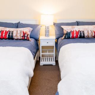 A cozy bedroom featuring twin beds with colorful pillows and a shared nightstand with a lamp.