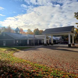 A building with a covered entrance surrounded by autumn trees and a cloudy sky.