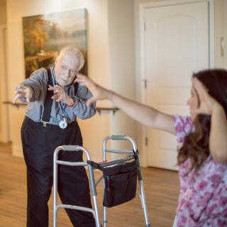 An elderly person engages in exercise with assistance from a caregiver indoors.