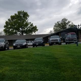 A lineup of vehicles parked on a grassy area near a building under cloudy skies.