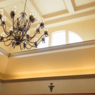 A luxurious interior featuring a chandelier hanging from a coffered ceiling with natural light streaming through an arched window.