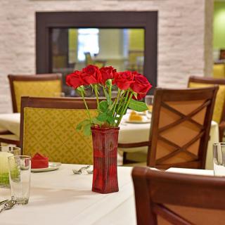 An elegantly set dining table with red roses in a vase, located in a restaurant interior.