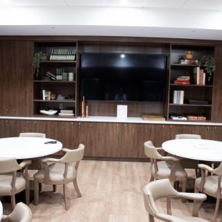 A modern conference room featuring circular tables, upholstered chairs, and a wall with wooden shelving surrounding a large TV.