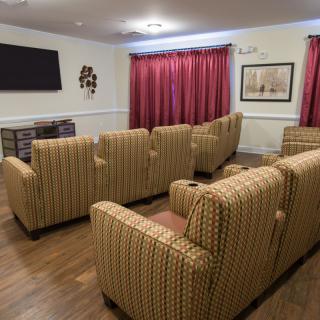 A cozy theater room with rows of comfortable chairs facing a large television, complemented by red curtains and warm lighting.