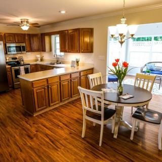 A cozy kitchen and dining area with wooden cabinets and flooring, featuring a table with chairs and a vase of flowers.