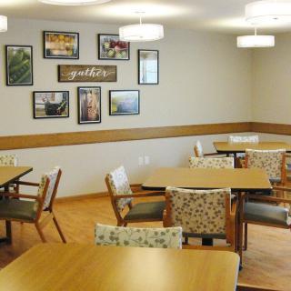A neatly arranged dining room with multiple tables and chairs, adorned with artistic wall decorations and warm lighting.