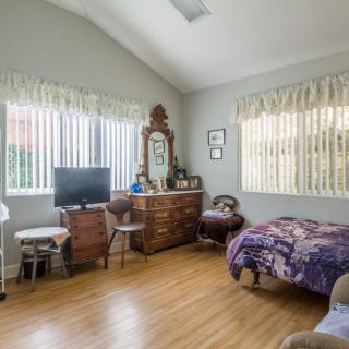 A cozy bedroom featuring a dresser with a mirror, a television, and hardwood flooring.