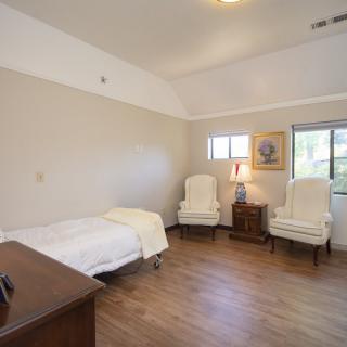 A minimalist bedroom with a single bed, two white chairs, and wooden flooring.