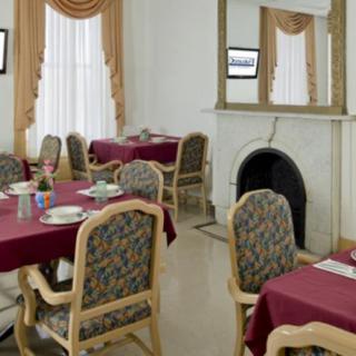 A well-decorated dining room featuring tables with red tablecloths and patterned chairs, complemented by a classic fireplace and elegant drapes.