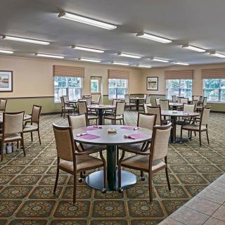A spacious dining area with multiple tables and chairs arranged on a carpeted floor, illuminated by overhead lighting.