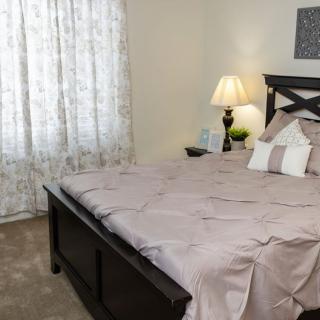 A cozy bedroom with a neatly made bed, bedside lamp, and floral curtains.