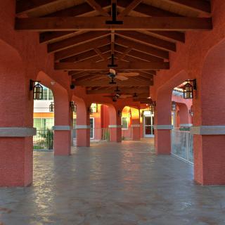 An outdoor corridor with red walls and wooden beams, featuring a series of arches and a tiled floor.