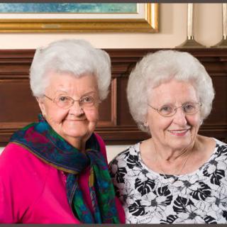 Two elderly women smiling together indoors.