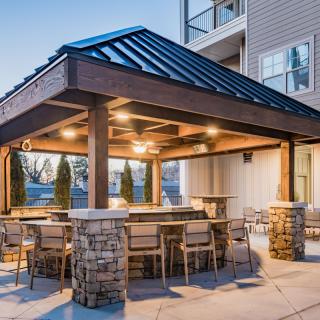 A well-lit outdoor patio area with a pergola and seating arrangements surrounded by stone pillars.