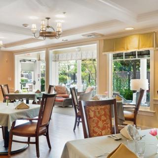 A well-lit dining area with neatly arranged tables and chairs, featuring large windows that provide natural light and a view of the outdoors.