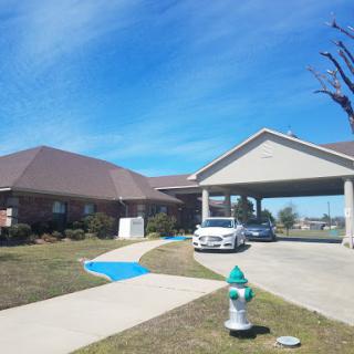 A tranquil residential scene featuring a house with a driveway, parked car, and a fire hydrant under a clear blue sky.