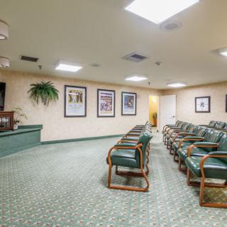 An empty waiting room with green chairs and carpet, adorned with framed pictures on the walls.