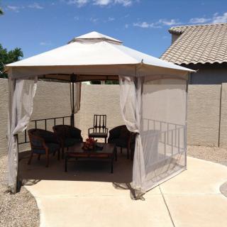 A cozy gazebo setup with chairs and a table in a sunny backyard.