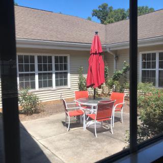 A sunny outdoor patio featuring a table surrounded by orange chairs and a red umbrella.
