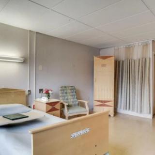 A clean and organized hospital room with a bed, wardrobe, and chair.