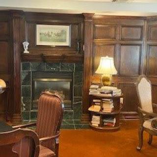 A cozy library room featuring a classic fireplace, wood paneling, and antique furniture.