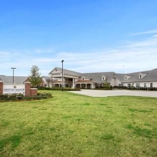 A large building with a driveway, surrounded by a well-maintained lawn under a clear blue sky.