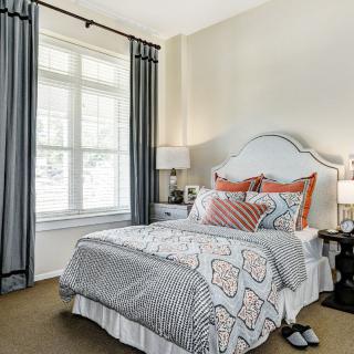 A cozy bedroom with a neatly made bed, decorative pillows, and natural light streaming through a large window.