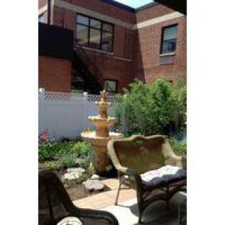 A tranquil garden patio with a fountain and seating area beside a brick building.
