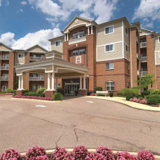 A multi-story hotel building with an entrance surrounded by landscaping under a partly cloudy sky.