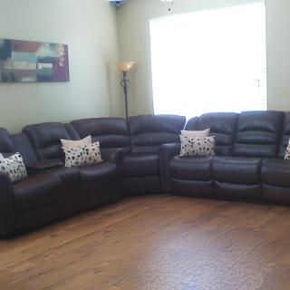 A cozy living room featuring a large dark leather sectional sofa adorned with decorative pillows, complemented by a floor lamp and wooden flooring.