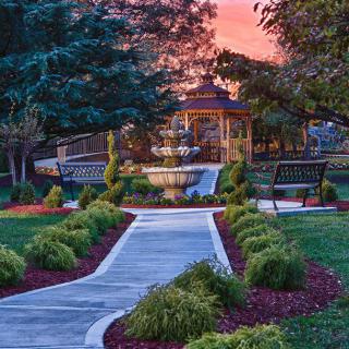 A beautiful garden pathway leading to a gazebo, surrounded by lush greenery and a stunning sunset sky.