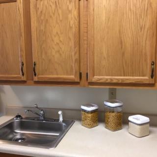 A kitchen scene with wooden cabinets, a sink, and storage containers on the countertop.