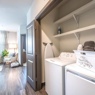 A modern laundry area with a washing machine, dryer, and shelving in a well-lit interior space.