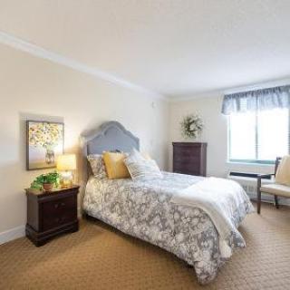 A cozy bedroom with a single bed, neatly arranged furniture, and soft lighting from a lamp on the nightstand.