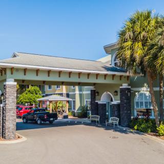 The entrance of a hotel with palm trees and a driveway under a clear blue sky.