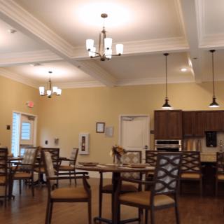 A cozy dining area with tables and chairs, featuring elegant lighting and a small kitchen section.