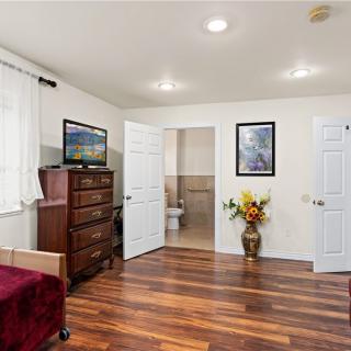 A cozy bedroom featuring hardwood floors, a dresser with a television on top, artwork on the walls, and a vase with flowers next to an open door.