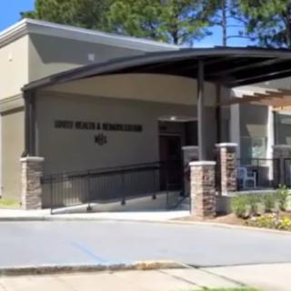 An exterior view of a modern building entrance surrounded by greenery and trees under a clear blue sky.