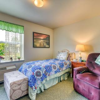 A cozy bedroom with a single bed, armchair, and a window bringing in natural light.