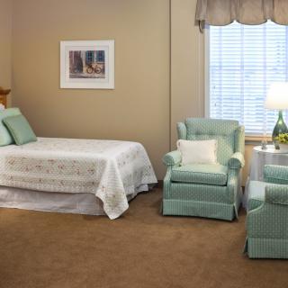 A cozy bedroom with a single bed, armchairs, and a window letting in natural light.
