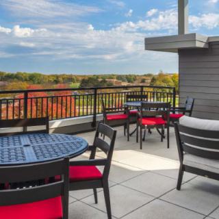 A rooftop patio with black chairs featuring red cushions and round tables overlooks a scenic landscape.