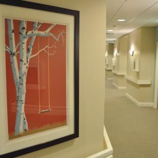 A hallway with a framed painting of a tree and swing on the wall.
