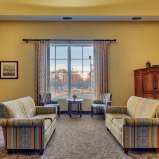 A cozy living room with two striped sofas facing each other, a large window with curtains, and a cabinet in the corner.