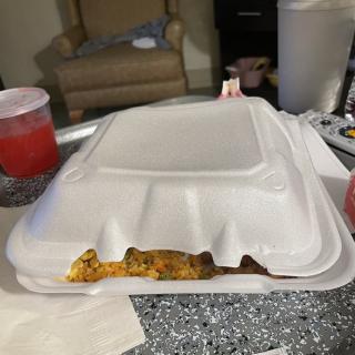 A styrofoam takeout container on a table with some food peeking out.
