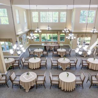 A spacious and elegant dining hall with round tables, chairs, and chandeliers.